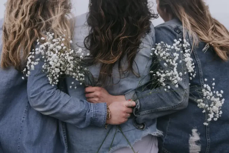 Three women in denim jackets embracing from behind, holding white baby's breath flowers